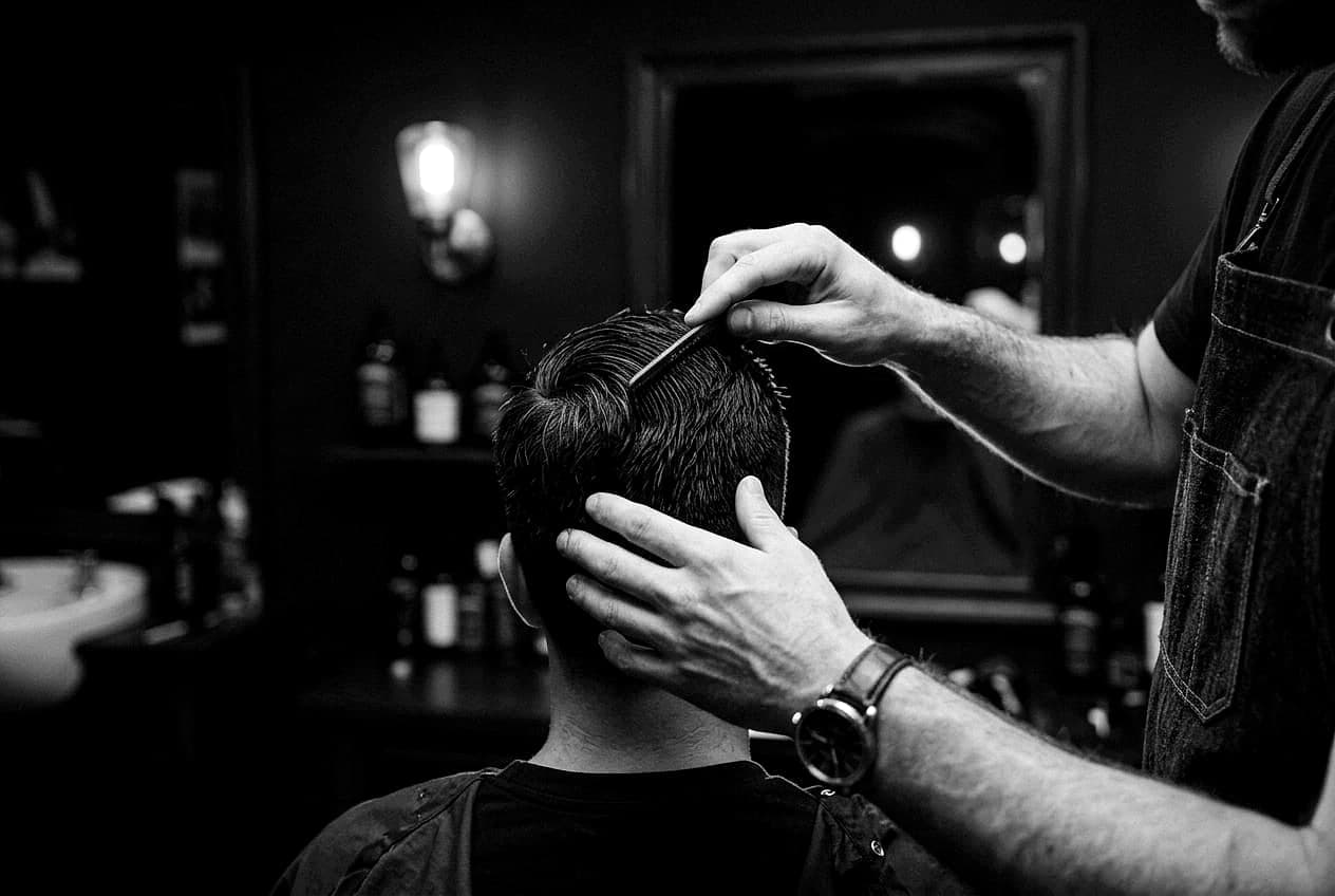 Coiffeur prüft den fertigen Schnitt mit dem Kamm